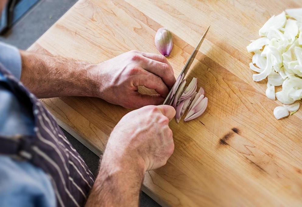 A chef chops shallots on a large cutting board