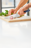 Using a blue Misen chef's knife to slice a radish on a wooden cutting board