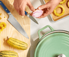 Using a Misen paring knife to cut a shallot next to a cutting board with a Misen Chef's Knife that has been used to prep delicata squash. The sliced squash then goes on parchment paper lined sheet pans, ready to roast. A sage enameled cast iron braiser can also be seen on the countertop.