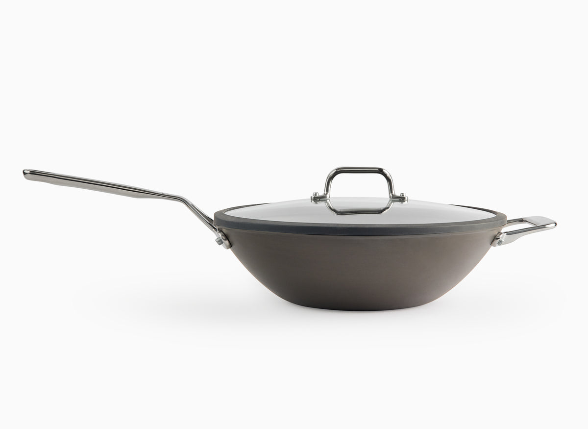 A side angle view of the Misen Carbon Steel Wok with its glass lid on, on a white background.