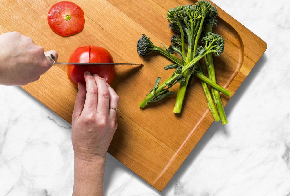 Best cutting board: Hands slice a tomato on the Misen Trenched Cutting Board