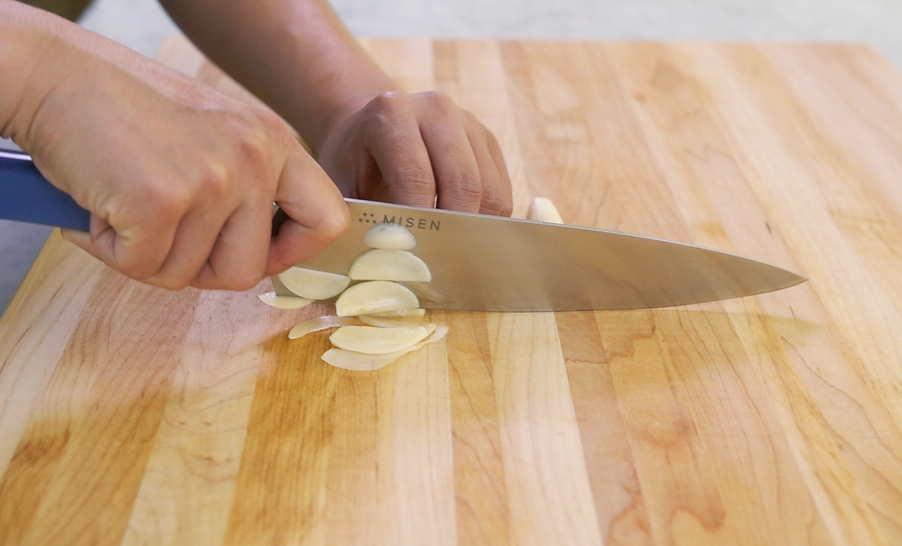 How to cut Garlic: Hands use a Misen Chef's Knife to slice garlic