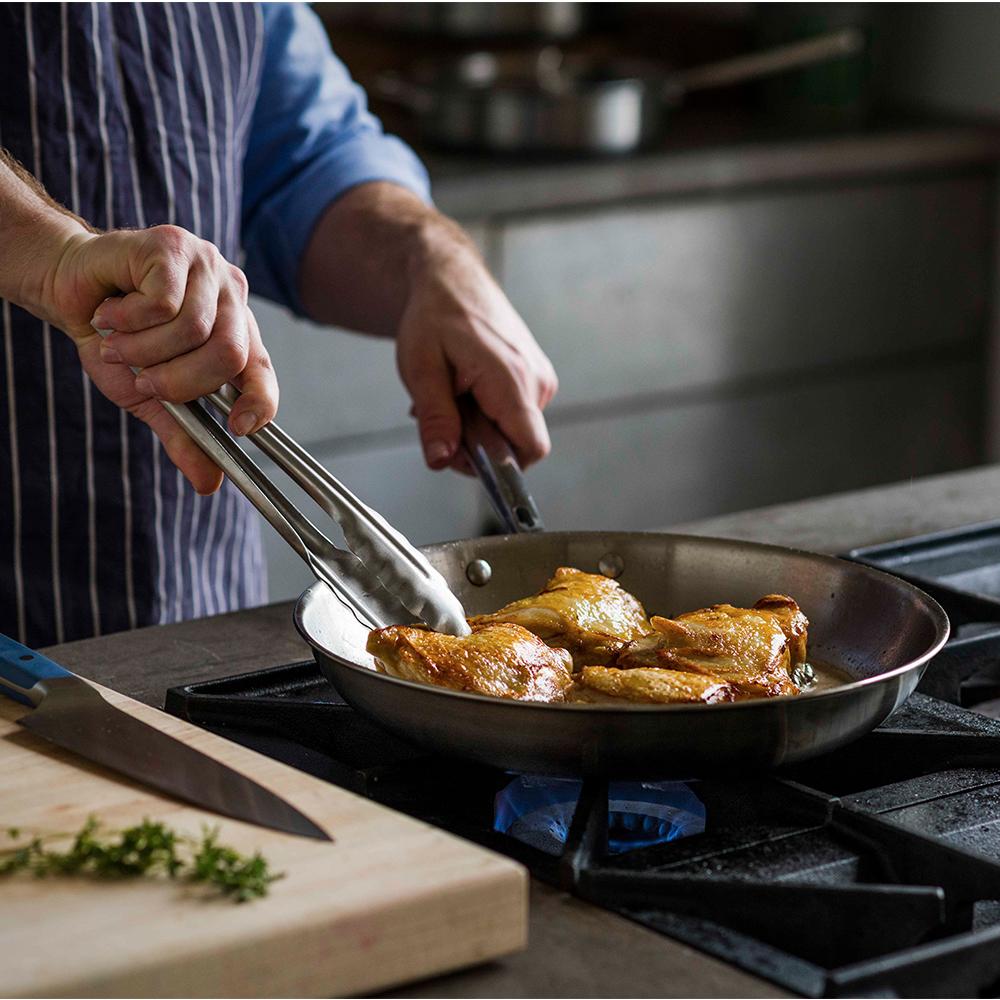 Man cooking chicken on a gas stove with a stainless steel pan, which is one example of the best cookware for gas stoves