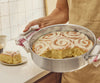 A chef holds a Misen Stainless Steel Rondeau filled with freshly-baked cinnamon rolls.