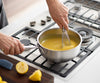 A hand uses a whisk to whip lemon curd in a Misen Stainless Steel Saucier on a stovetop.