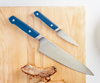 Using a blue 2PC Misen Knife Set to cut ribs atop a wooden cutting board