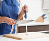Honing a Misen Chef's Knife with the Misen Honing Rod atop a wooden Misen cutting board, wearing a blue Misen apron