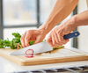 Using a blue Misen Chef's Knife to slice radishes atop a wooden Misen cutting board