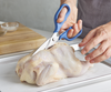 Using a pair of blue Misen Kitchen Shears to prep a chicken