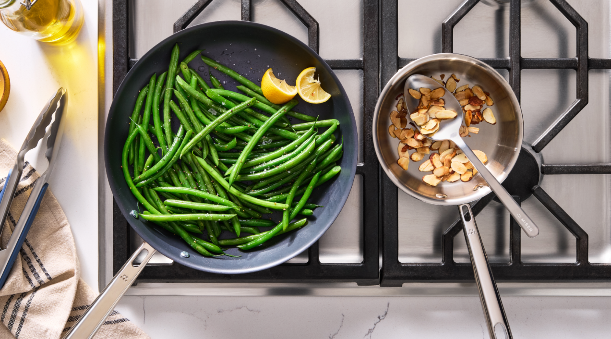 Sautéed green beans with lemon in nonstick skillet alongside toasted almonds in stainless saucepan on gas stovetop