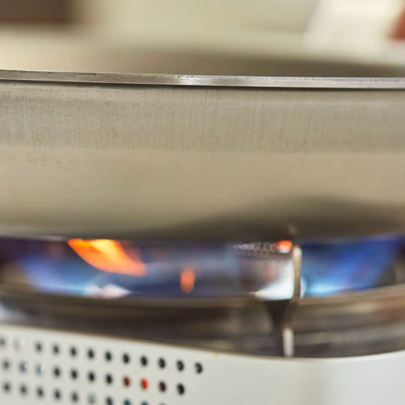 Gas stove burner with blue and orange flames heating stainless steel pan