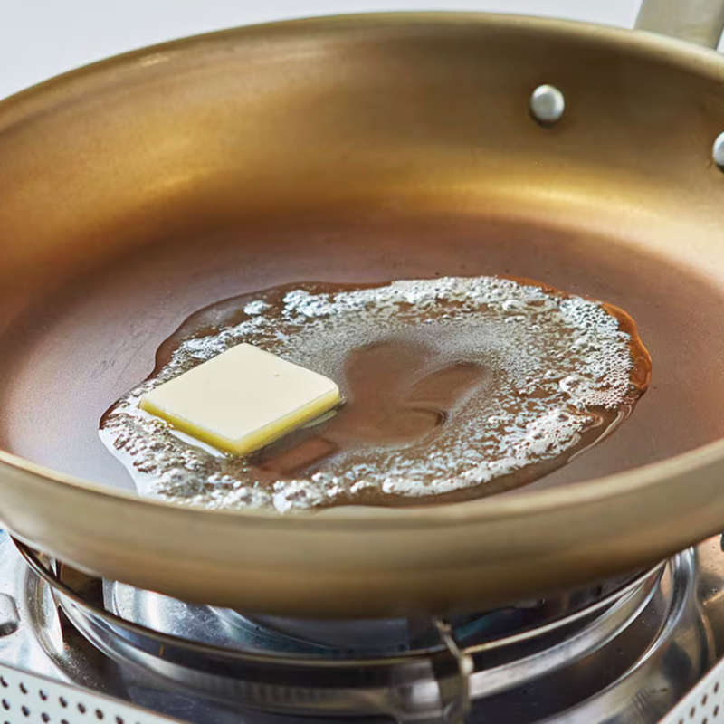Butter melting in a golden copper skillet on a gas stovetop