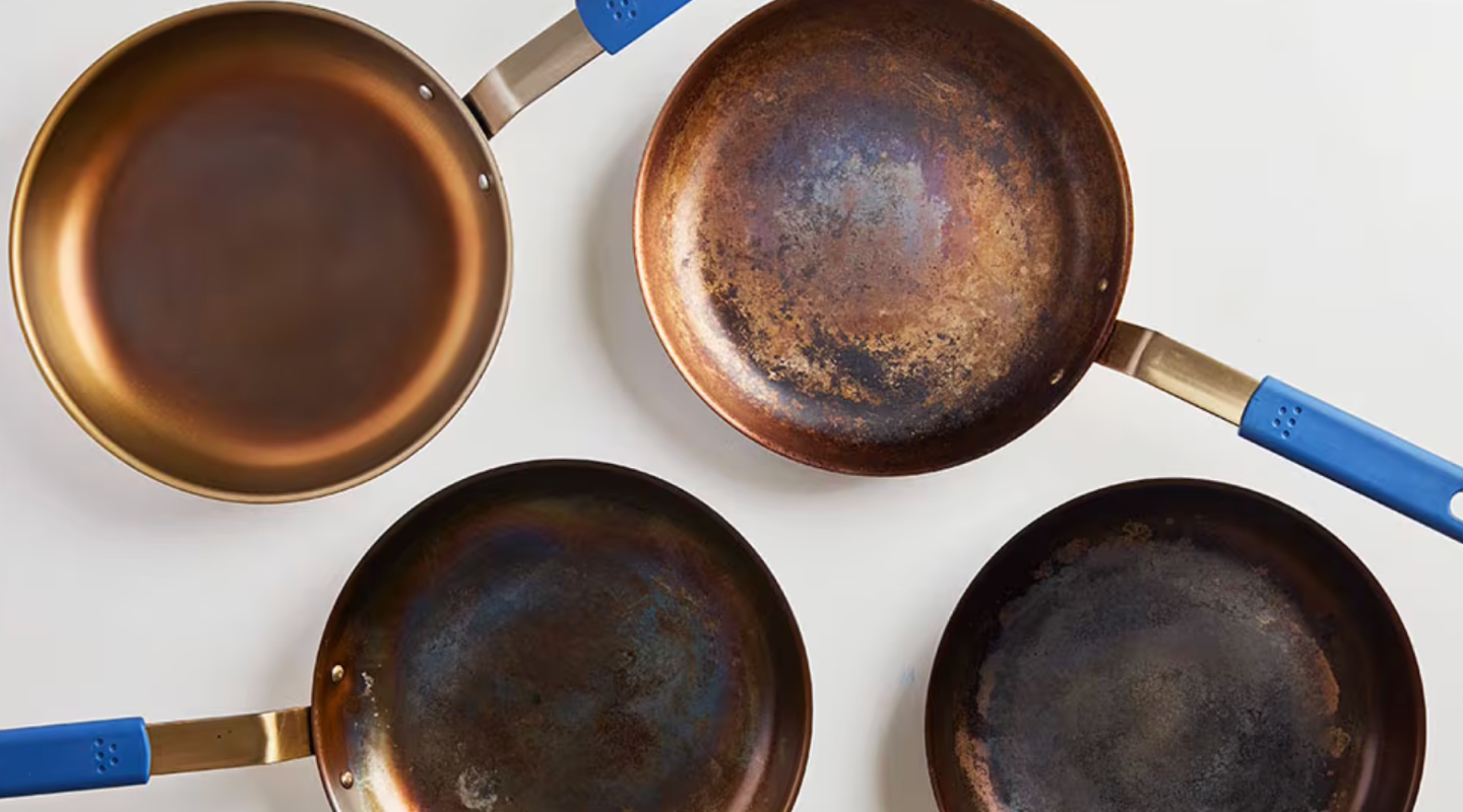 Four copper and carbon steel skillets with blue silicone handles showing seasoning progression from new to well-used