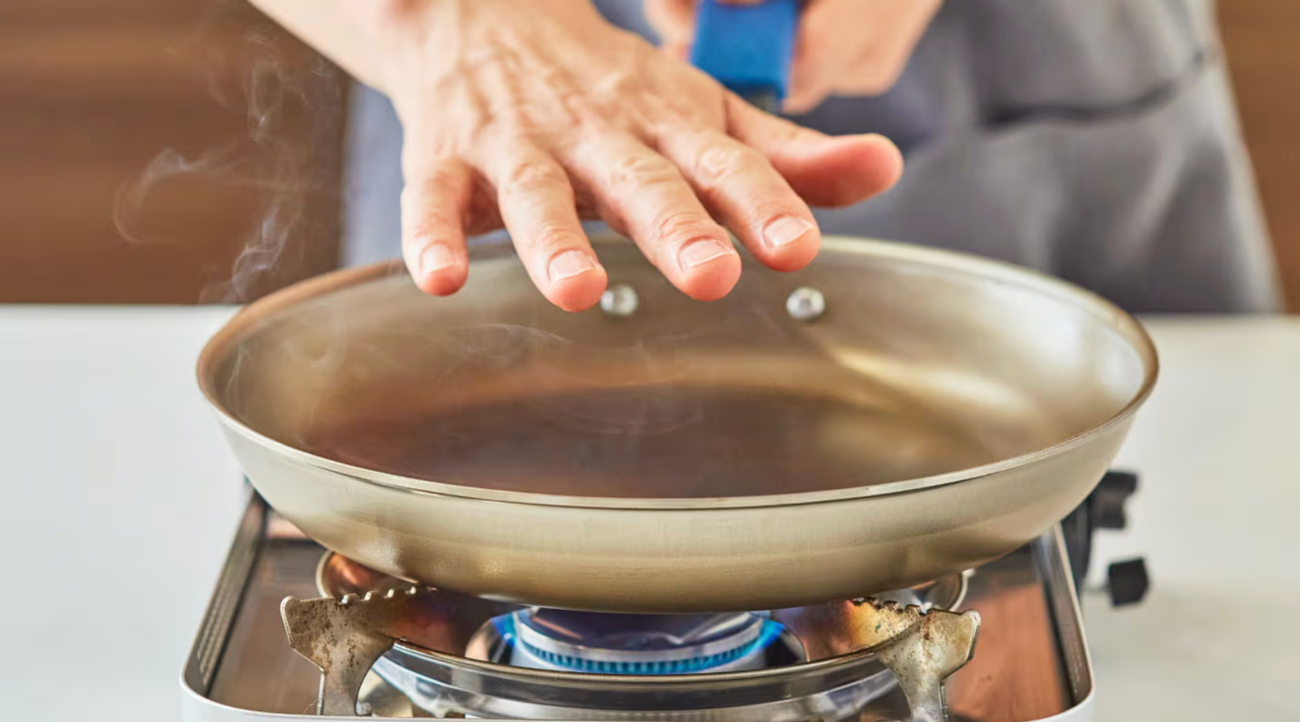 Person checking heat of stainless steel pan on gas burner with steam rising