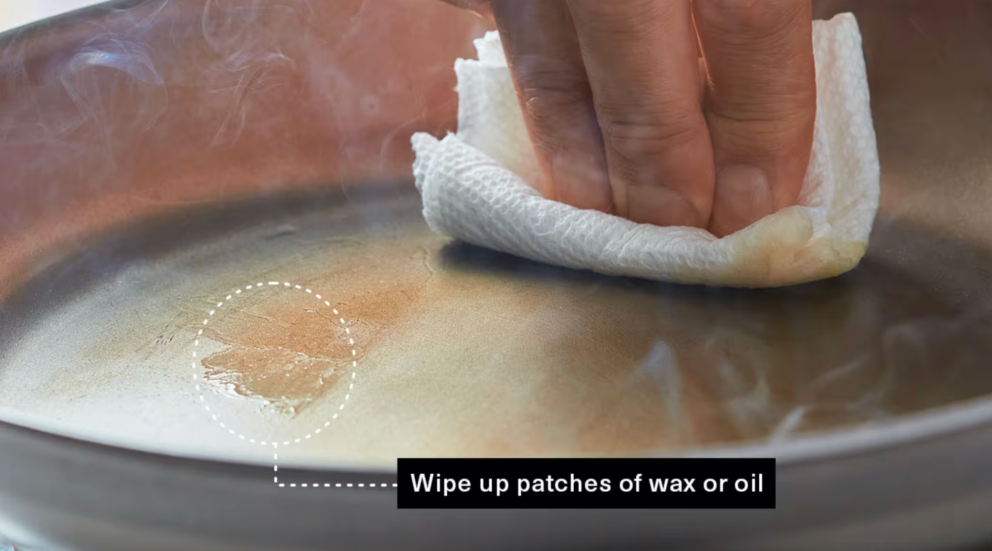 Wiping oil patches from a hot carbon steel pan with paper towel during seasoning