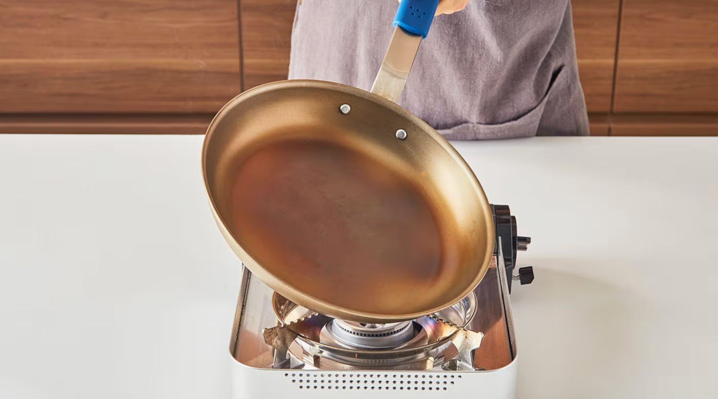 Carbon steel pan being seasoned over gas burner with heat mitt