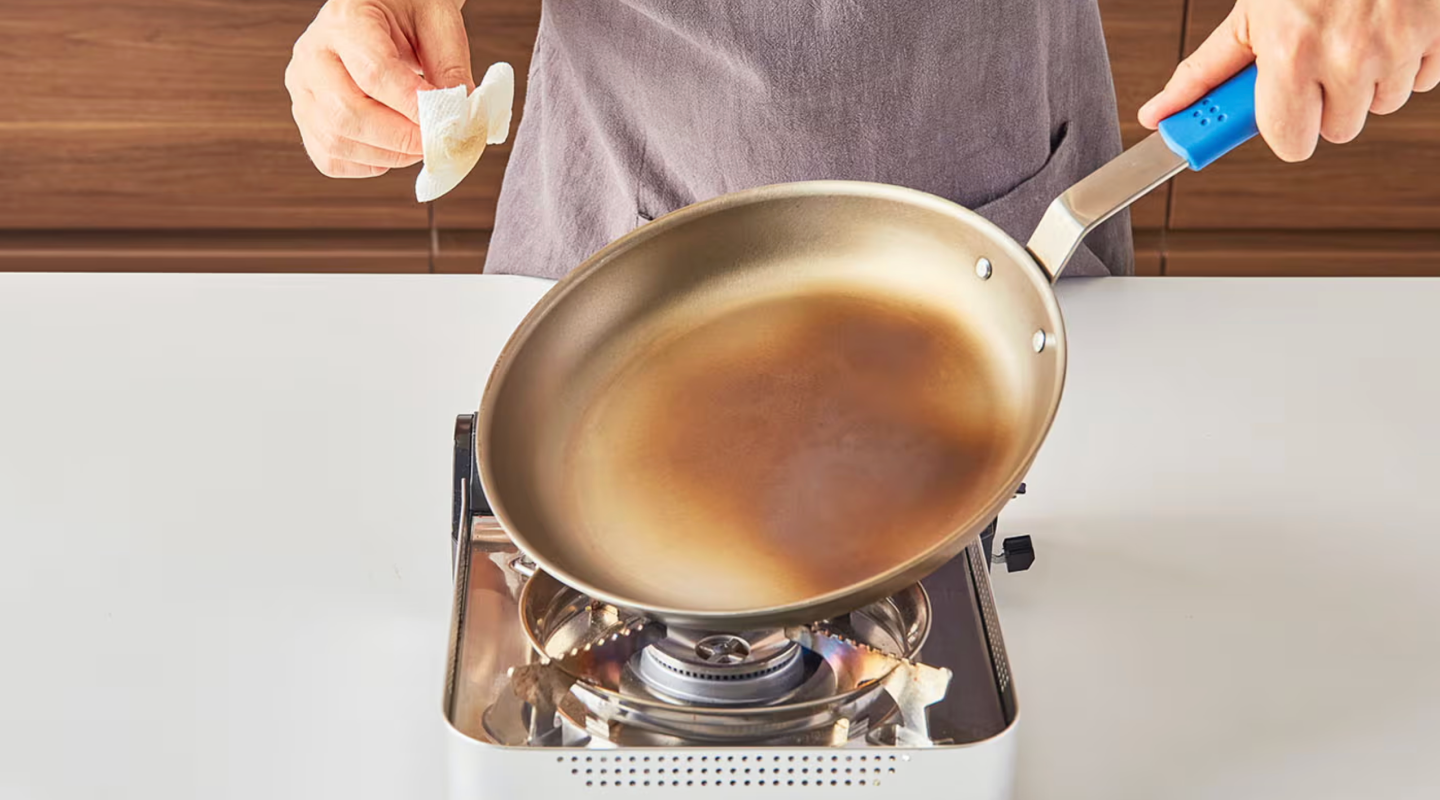 Person seasoning a carbon steel frying pan on a portable gas stove