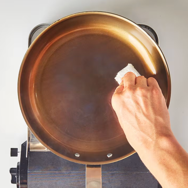 Hand wiping carbon steel pan with paper towel to season cookware