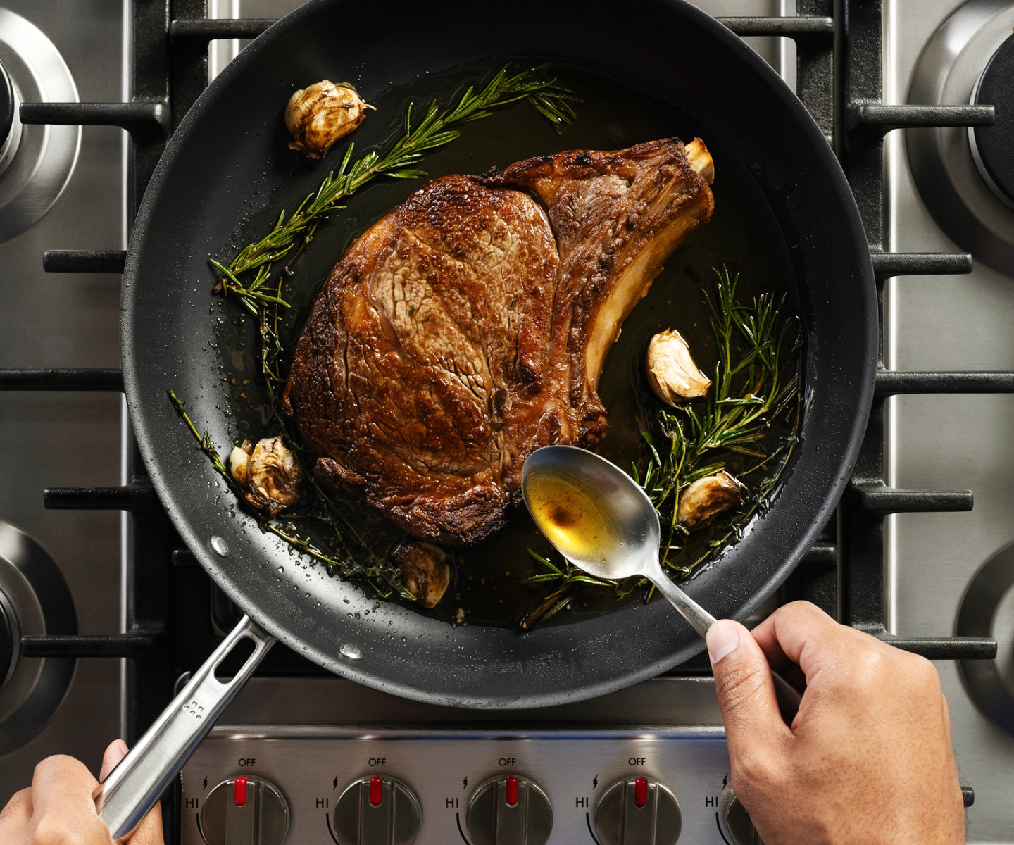 Pan-searing ribeye steak with rosemary, garlic, and butter basting on gas stovetop