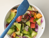Mixing a fruit salad with a blue Misen spatula in a white bowl