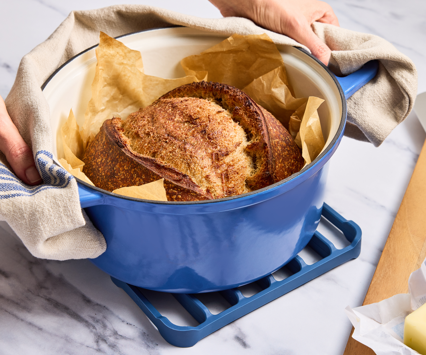 Freshly baked sourdough bread in a blue enameled Dutch oven on marble countertop