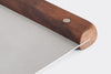 A close-up view of the Misen Bench Scraper’s walnut handle, on a white background, with part of the metal blade visible.