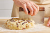 A pair of hands uses a Misen Bench Scraper with walnut handle to divide scone dough into even sections, working atop a Misen Wood Cutting Board.