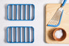 A bird’s eye view of two blue Misen Silicone Roasting Racks next to a Misen Fish Spatula and a bowl of salt, both atop a cutting board.