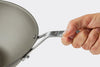 A hand holds the handle of a Misen Carbon Steel Wok on a white background. Half of the wok is visible.