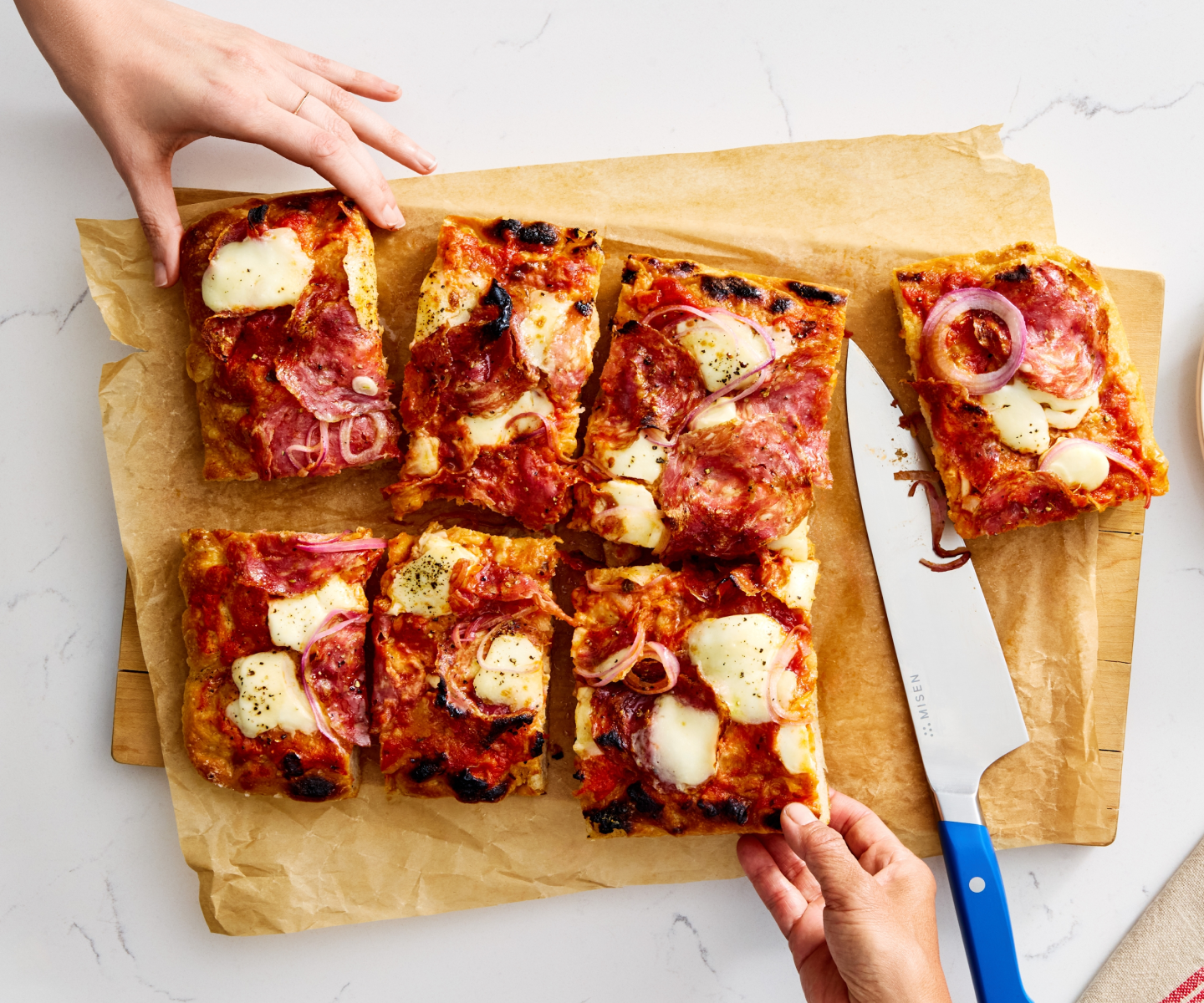 Homemade sheet pan pizza cut into squares with salami, mozzarella, and red onion on parchment paper