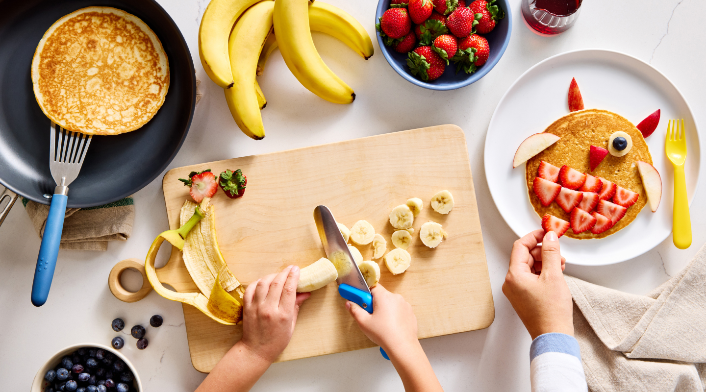 Hands decorating a fun fruit pancake with strawberries and banana slices for kids breakfast