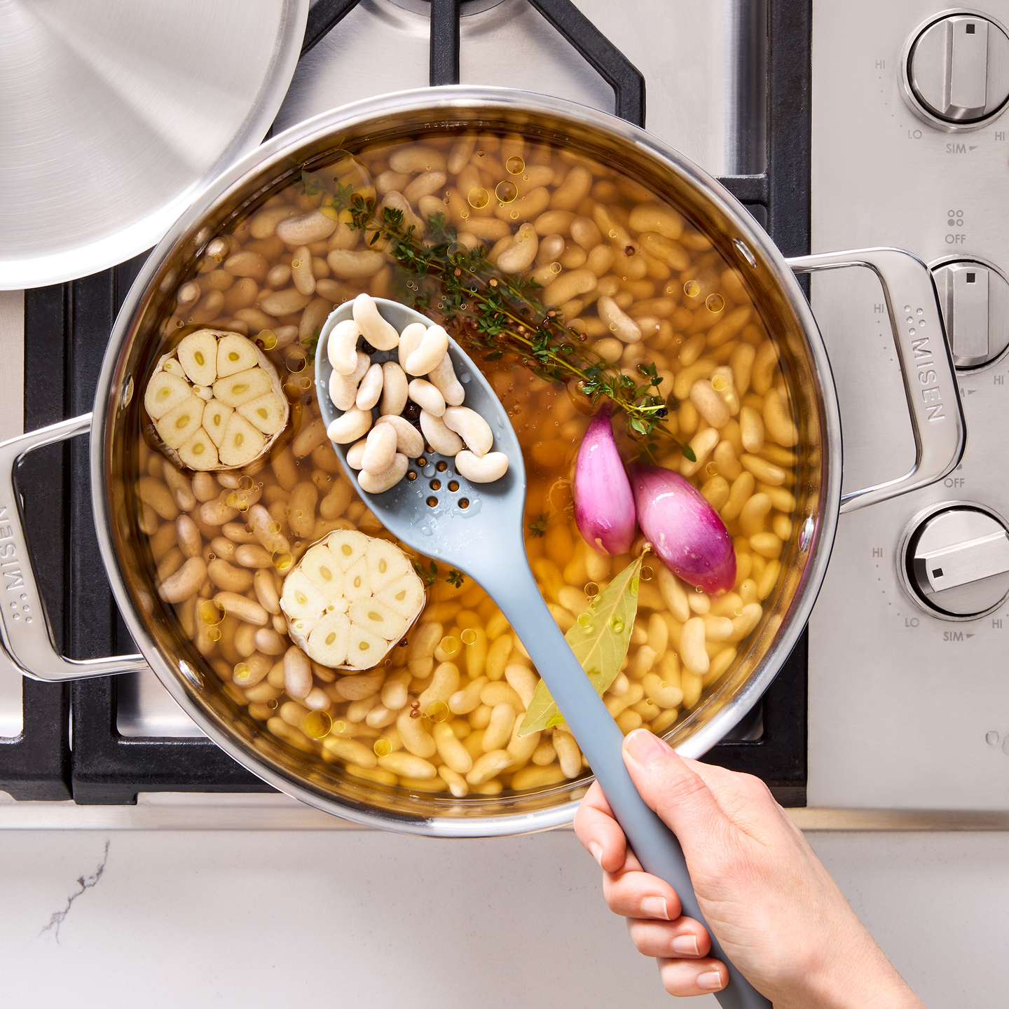 White beans simmering in stainless steel pot with garlic, shallots, thyme, and bay leaf