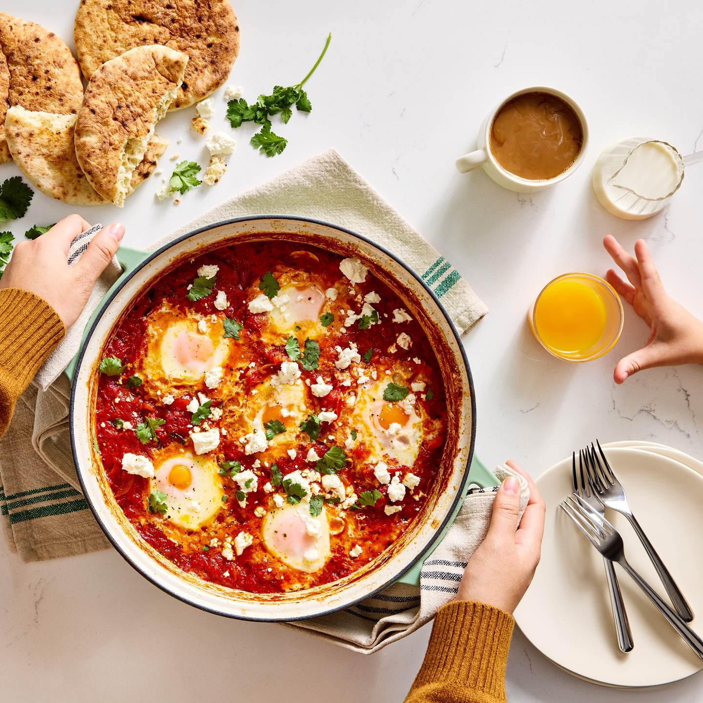 Shakshuka with poached eggs, feta cheese, and fresh cilantro served in a rustic skillet with pita bread