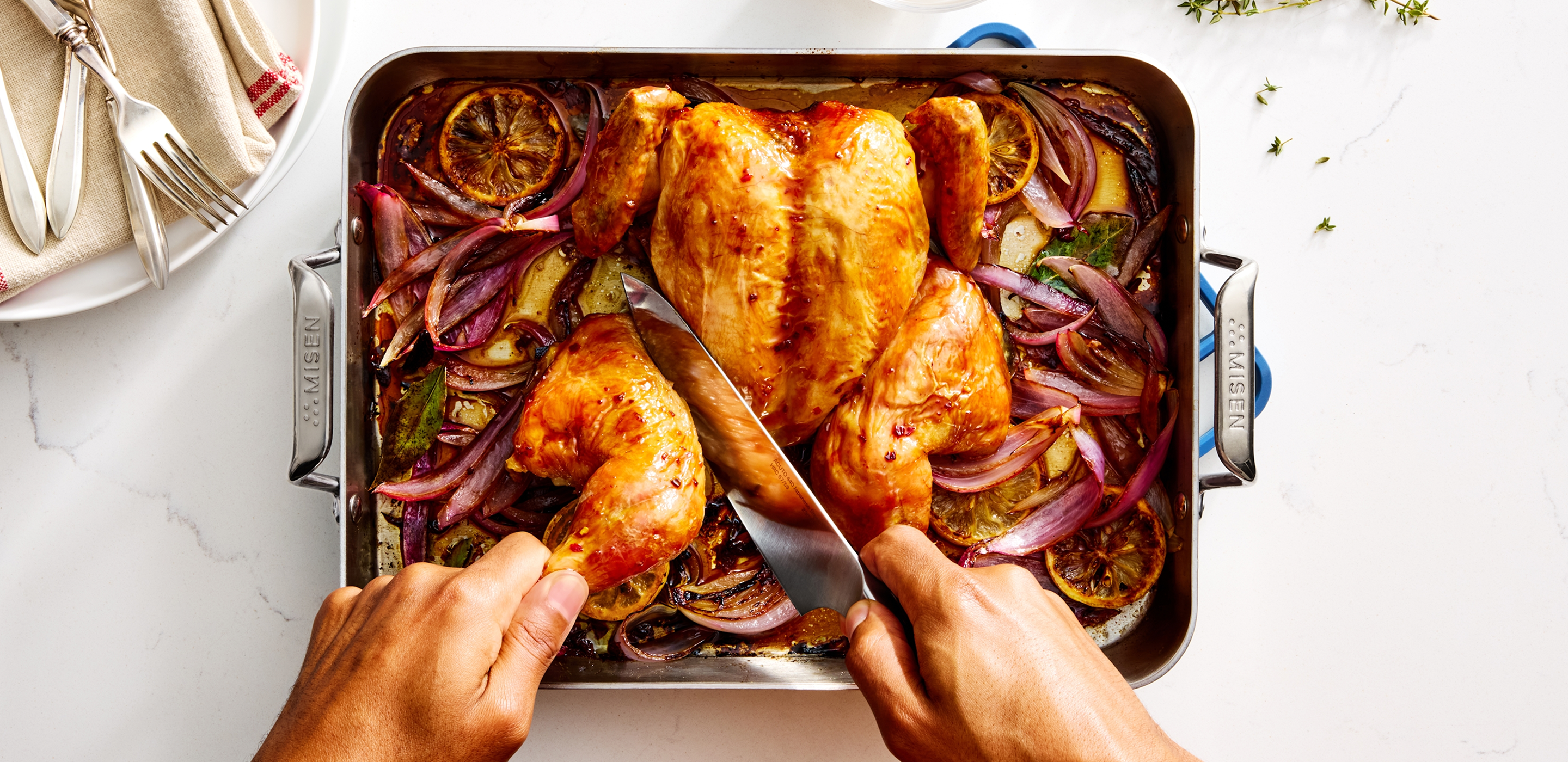Hands carving roasted spatchcock chicken in Misen roasting pan with caramelized lemon and red onion