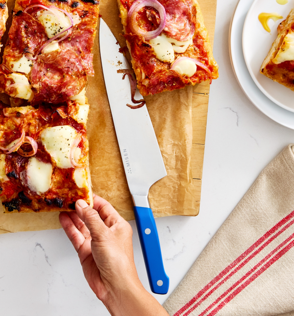 Misen chef's knife with blue handle cutting homemade Detroit-style pizza on wooden board