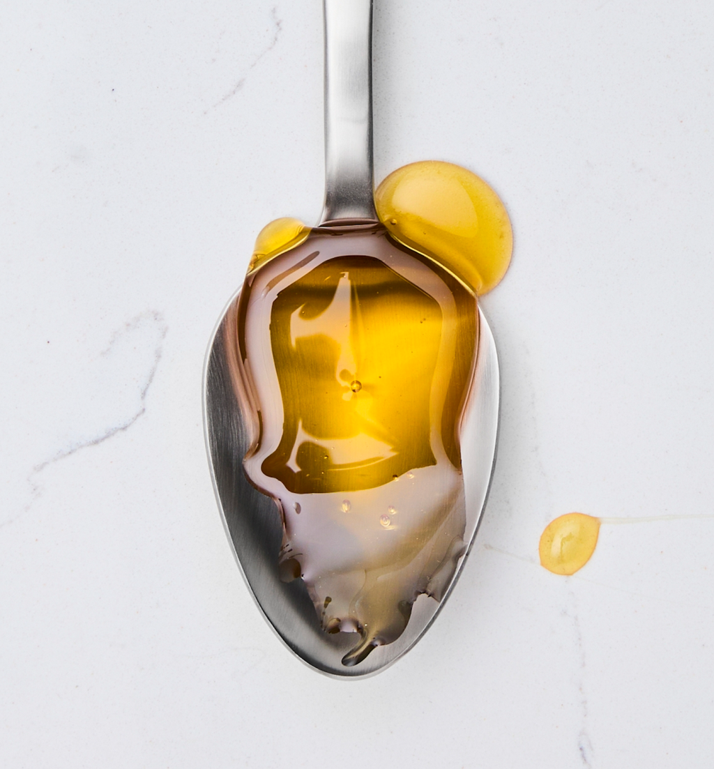 Golden honey or olive oil drizzled on a stainless steel spoon on marble surface