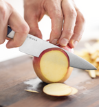 Misen paring knife slicing a fresh red apple on a wooden cutting board