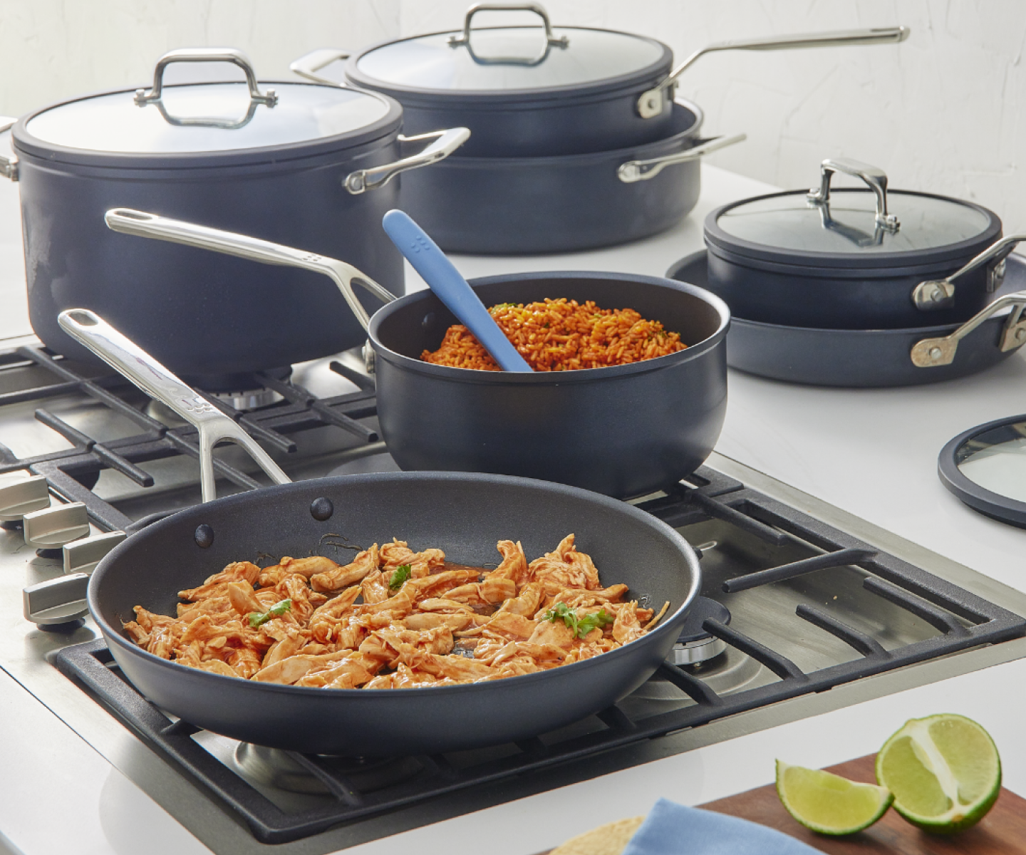 Navy blue nonstick cookware set with shredded chicken skillet and Spanish rice saucepan on gas stove