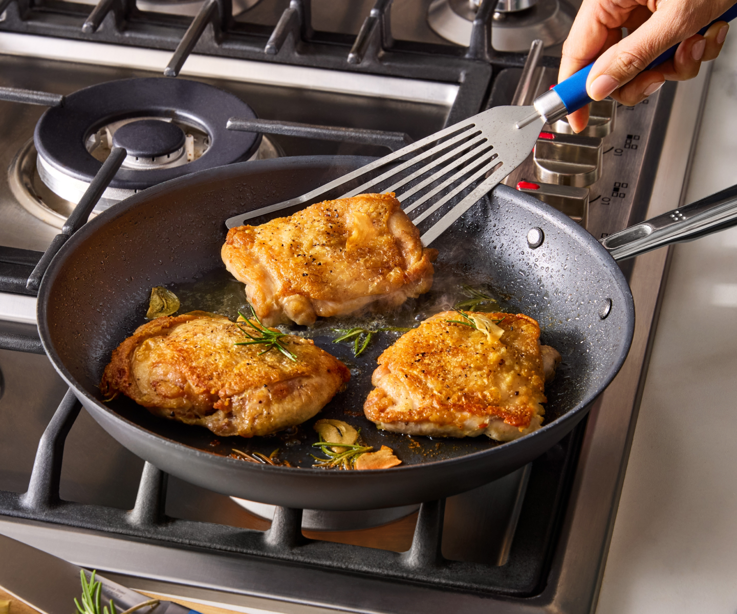 Golden brown pan-seared chicken thighs cooking in skillet with rosemary and garlic