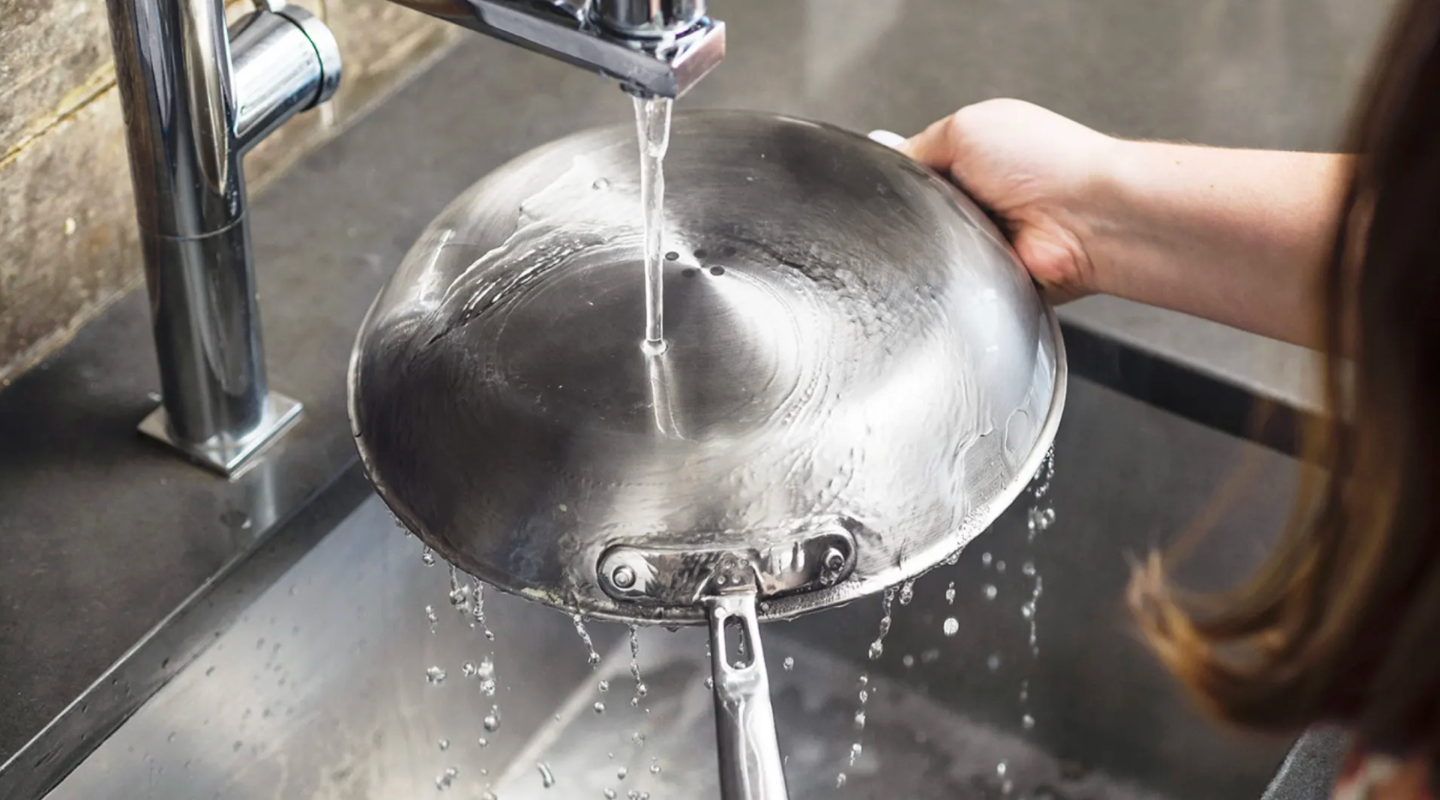 Rinsing stainless steel frying pan under kitchen faucet