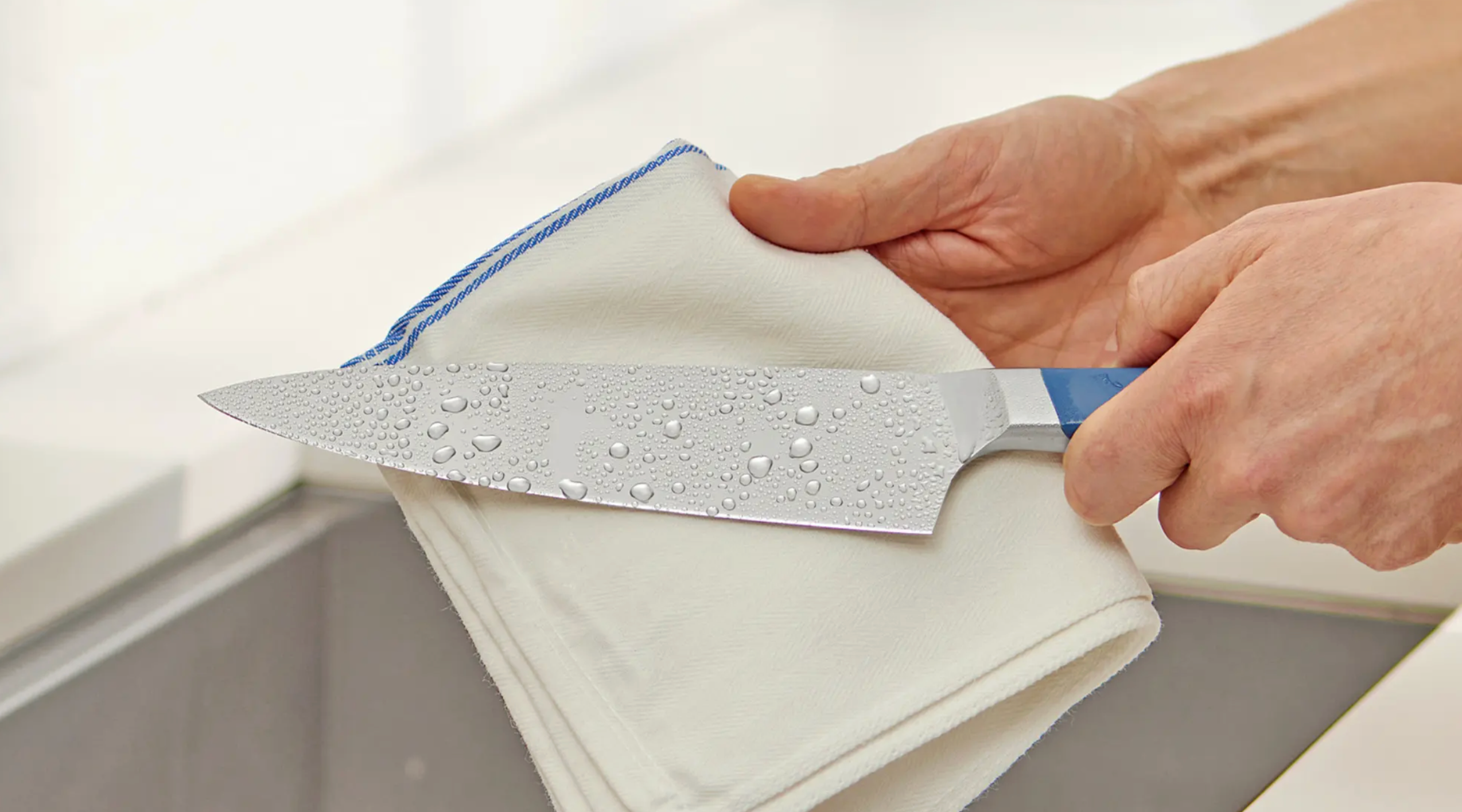 Hand drying a chef's knife blade with a white kitchen towel after washing