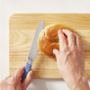 Using a blue, Misen, five inch, short serrated knife to cut a plain bagel in half
