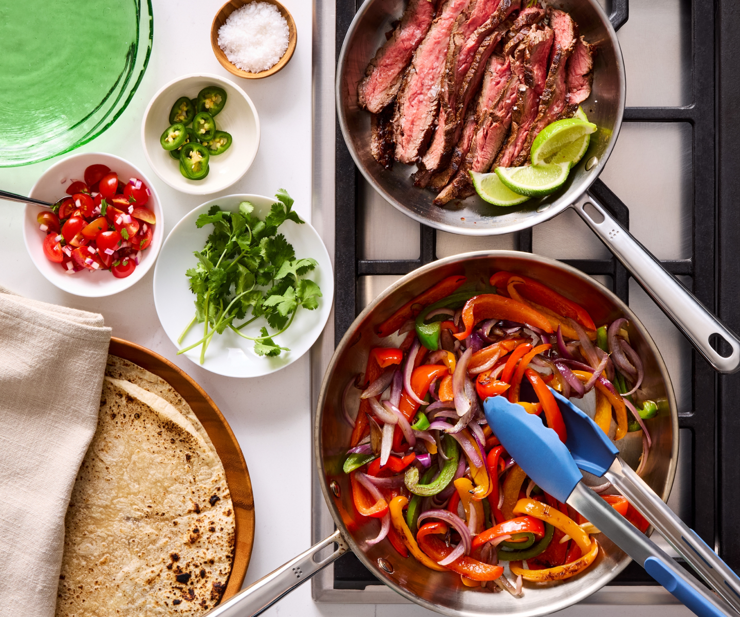 Steak fajitas preparation with sautéed peppers and onions, sliced skirt steak, tortillas, and fresh toppings
