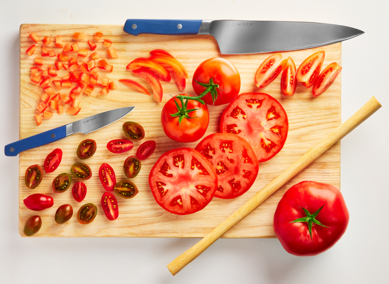 Demonstrating different knife cuts with a blue Misen Chef's Knife and a tomato