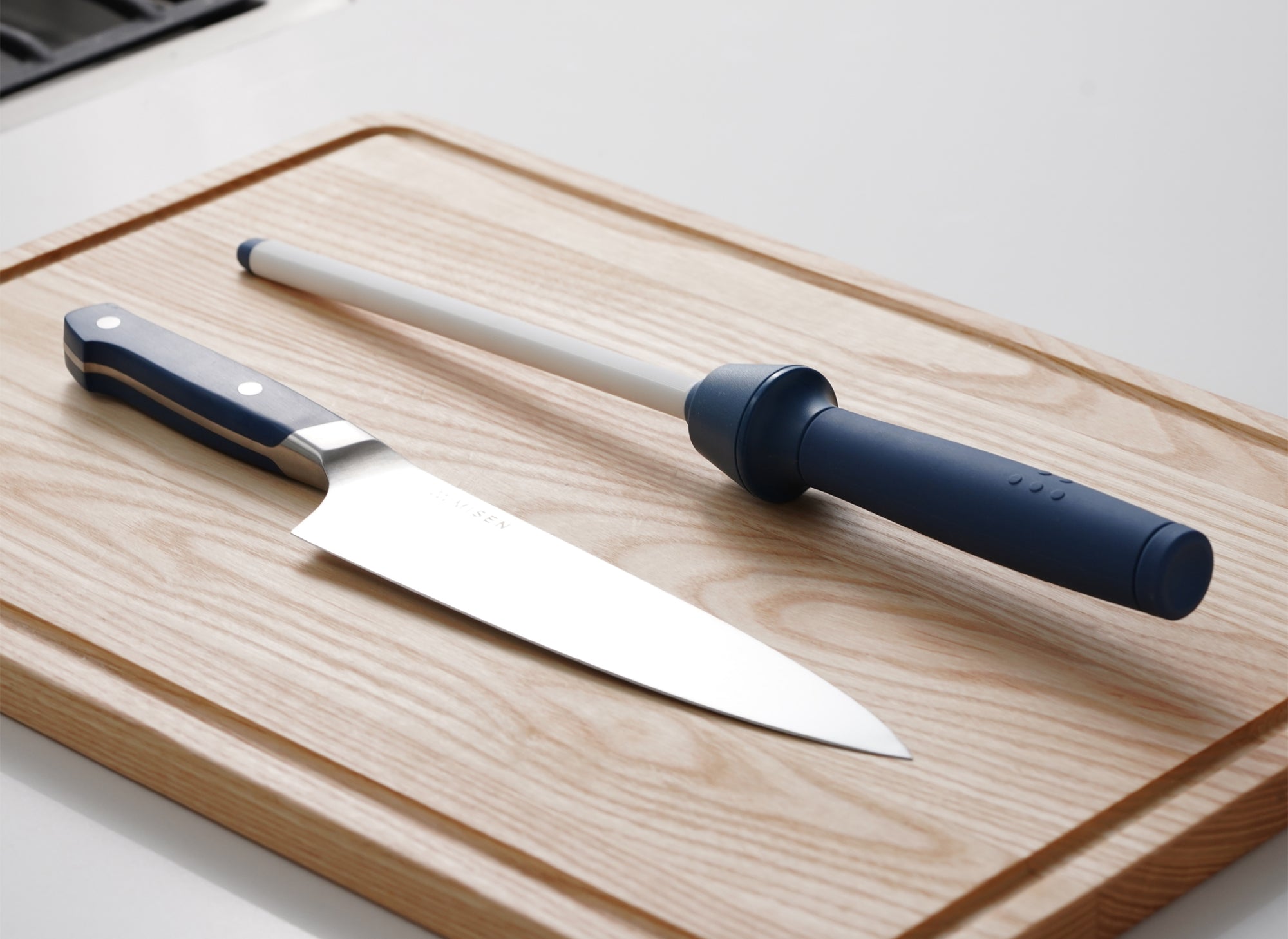 A Misen Honing Rod and a Misen Chef's Knife on top of a large Misen Cutting Board.