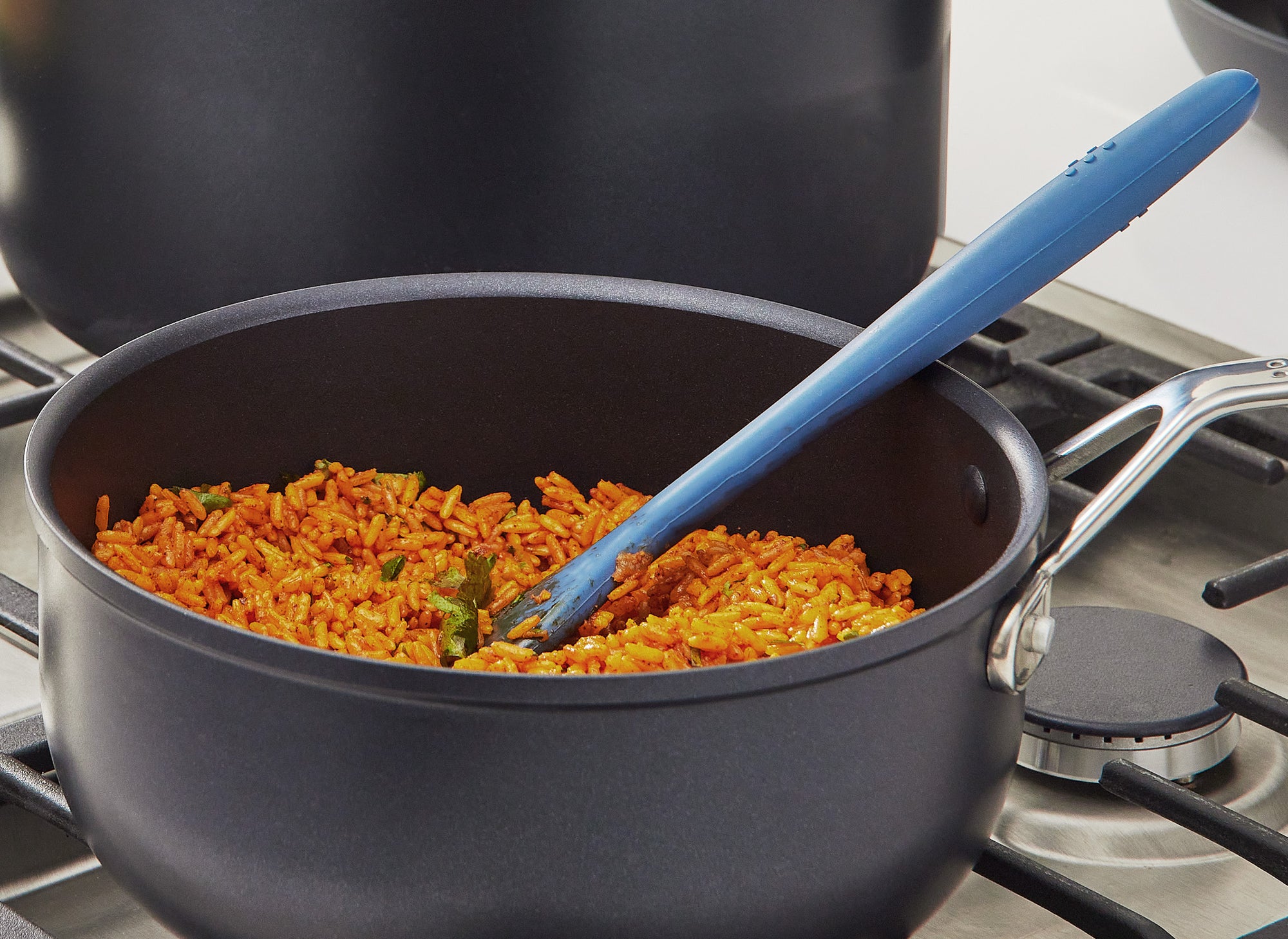 A Misen 3 QT Nonstick Saucier sits on a stovetop, filled with seasoned rice. A blue Misen Silicone spatula rests inside the Saucier.