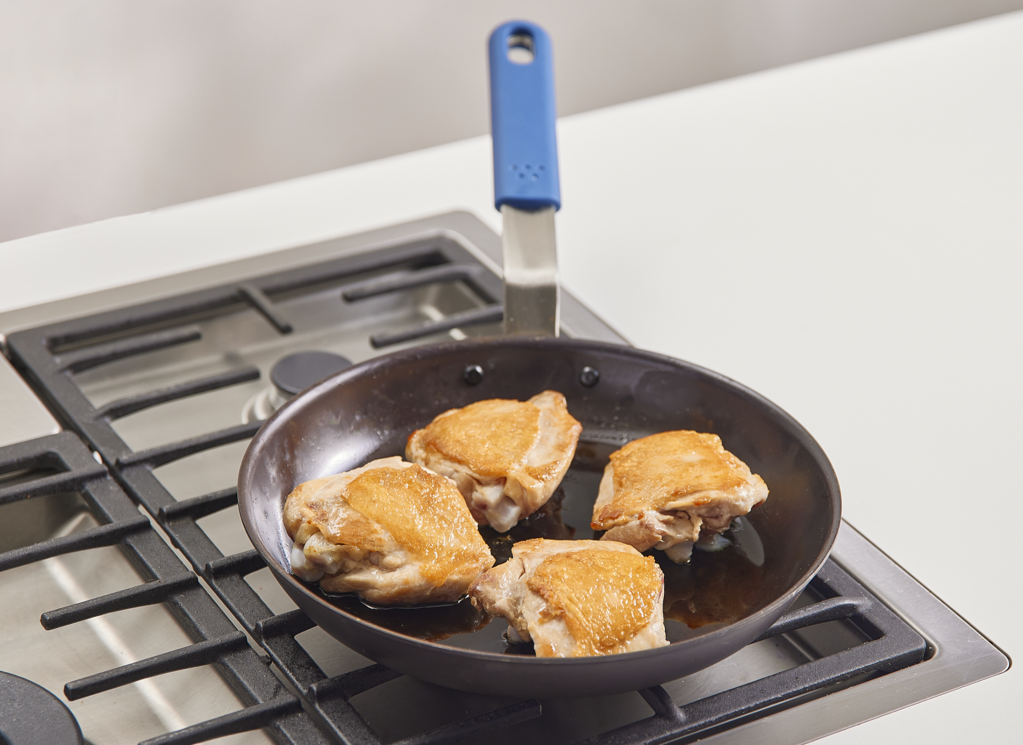 Frying four chicken thighs in a Misen Pre-Seasoned Carbon Steel Pan.