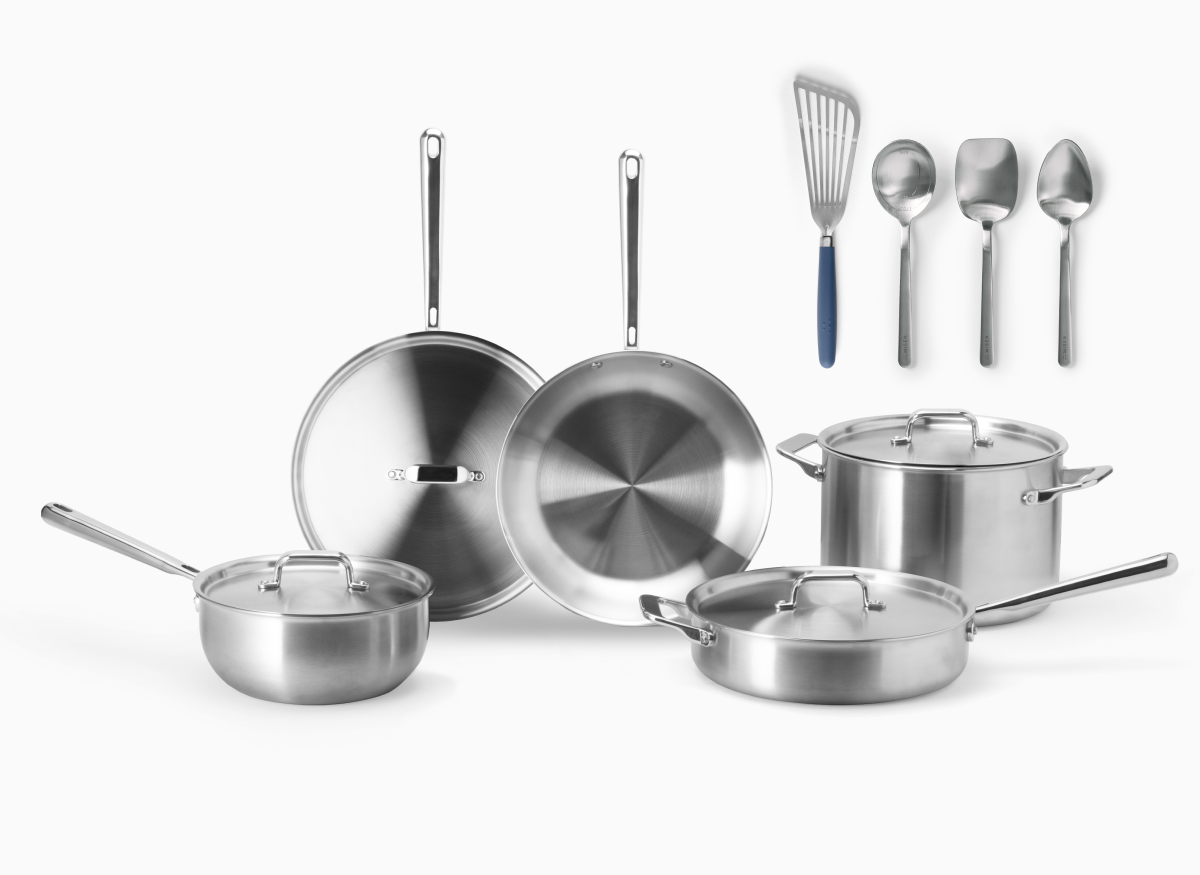 The image displays a set of Misen stainless steel cookware and accompanying Misen cooking tools. The cookware includes two frying pans, a sauté and saucier with lids, and a large 8 qt stockpot, all featuring a shiny, metallic finish. The tools are shown on the right side of the image, consisting of what appears to be a slotted stainless steel fish spatula with a blue handle, a measuring chef spoon, a scraper chef spoon, and a plating chef spoon.