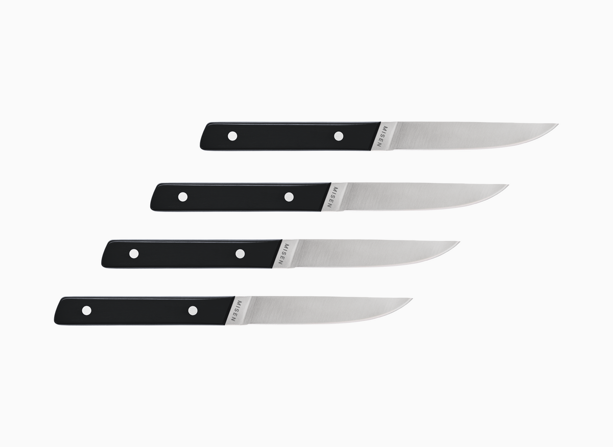 Set of four straight edge Misen ACUTO steak knives with black handles on a white background