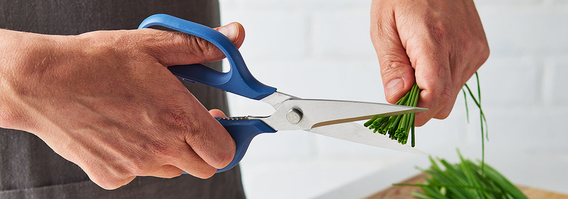 A hand uses blue Misen Shears to chop a handful of chives.